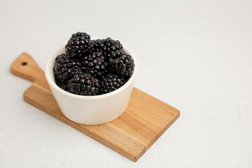 Fresh blackberries in a white bowl on a wooden cutting board