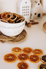 Dried orange slices in a decorative bowl placed near small white houses on a wooden surface