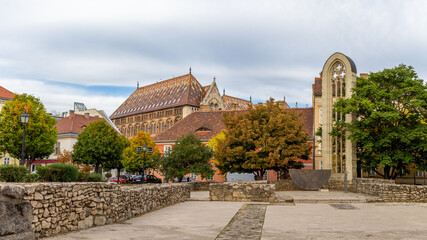 Fototapeta premium Panorama of Mary Magdalene Church foundation with recreated Gothic window, autumn trees, and historic Buda rooftops including Zsolnay-tiled National Archives. Budapest, Hungary.