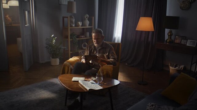 Elderly man gazes at black-and-white photos in half-light room