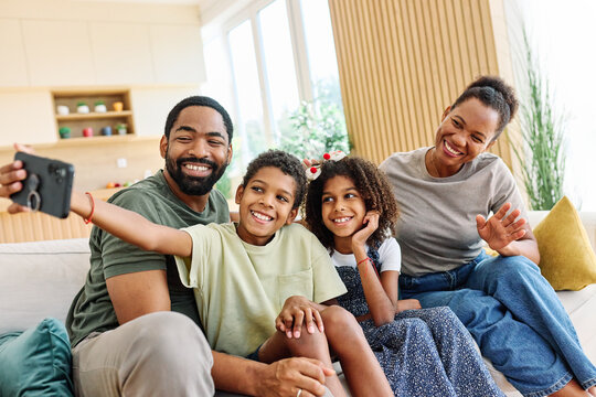 Portrait of a happy black family mother father and kids taking selfie with mobile phone having fun  at home on couch