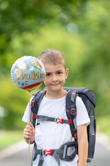 Fr&ouml;hlicher Erstkl&auml;ssler mit Schulranzen und Ballon &bdquo;Schulkind&ldquo; &ndash; Portr&auml;t eines Jungen am ersten Schultag, Einschulung, Schulanfang, Grundschule, Bildung, deutsche Tradition