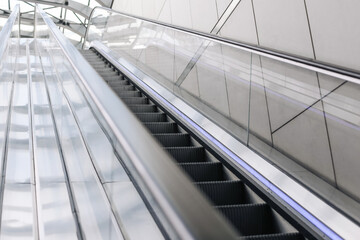 Fototapeta premium Modern escalator going up in glass building. Perspective view with reflections on metal and glass panels. Urban architecture design for transport. Empty moving stairs.