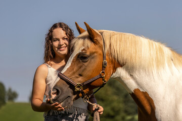Young woman bonding with Haflinger crossbreed pinto mare outdoors in summer