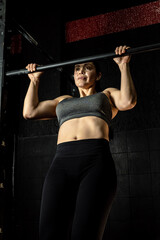White Latina woman doing pull-ups on an iron bar in a gym during an exercise routine, studio shot. Concept of exercise, gymnastics, sports, health, and wellness.