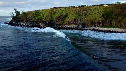 Surfers riding waves near a lush green cliff on a beautiful tropical island coastline