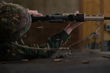 Military trainee in prone firing position with rifle and scattered ammunition on ground