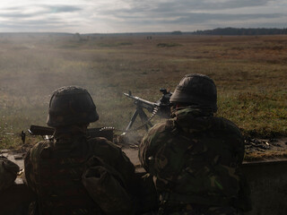 Fototapeta premium Military personnel operating machine gun from field position overlooking training area