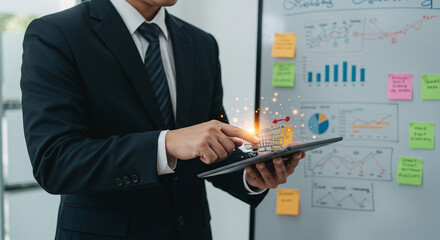 A businessman in a suit interacts with a digital shopping cart on a tablet in front of a whiteboard