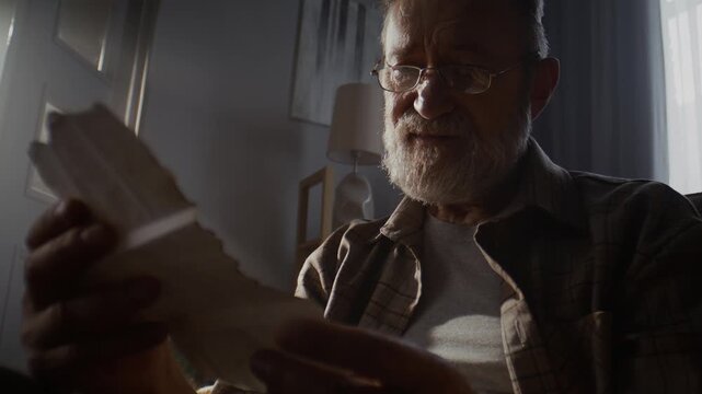Lonely pensioner sits and studies words on aged sheet of paper