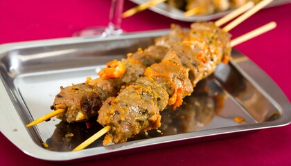 Golden skewers of seasoned meat, garnished with peppers, sit on a gleaming metal tray, a perfect presentation for a gourmet meal.