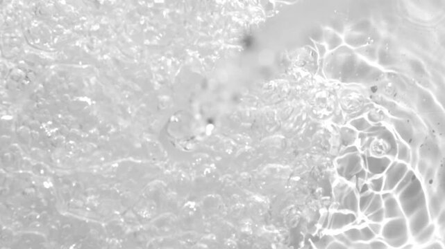 Close-up of water bubbles and shimmering light reflections on a smooth surface. High contrast and clarity emphasize fluid textures and glistening highlights