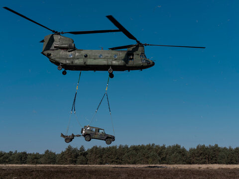 Chinook helicopter airlifting military vehicle using sling load system during daylight operations