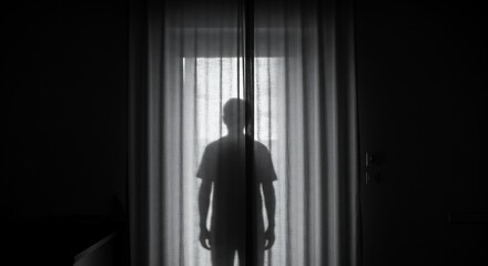 A persons silhouette stands behind a curtain in front of a window the scene is dark