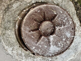 Close up of old rusty round metal hatch on weathered concrete surface