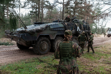 Female soldier observing armored vehicle operations in forest tactical environment