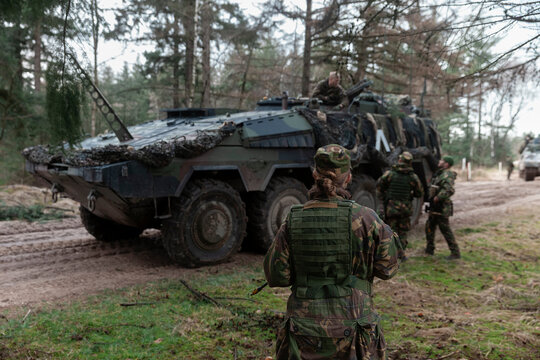 Female soldier observing armored vehicle operations in forest tactical environment