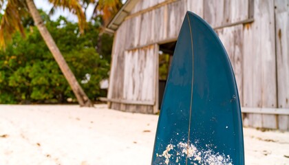 A teal surfboard rests against a weathered wooden building on a sandy beach.