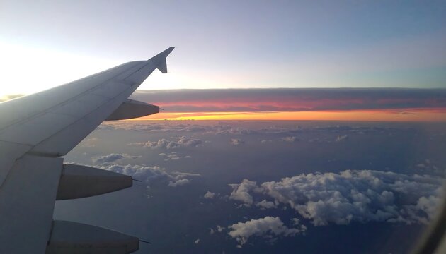 A view from an airplane window reveals a stunning sunrise over a blanket of clouds.