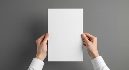 A person holding a blank white sheet of paper against a gray background in portrait orientation