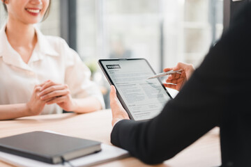 Young woman smiling during job interview with recruiter holding resume on digital tablet in modern office