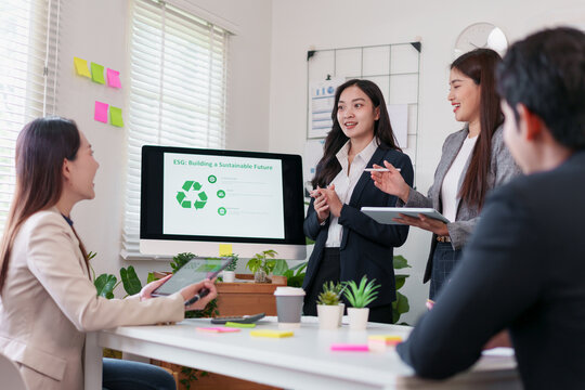 Young Asian business professionals in formal attire present ESG sustainability strategy with confidence and teamwork in modern office, using digital devices and large screen