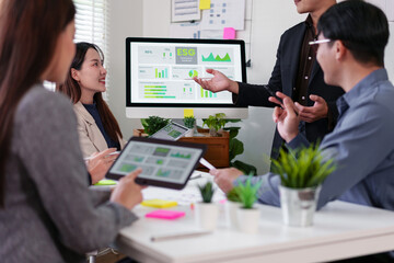 Business team meeting in modern office, discussing ESG data and sustainability strategy with digital devices, diverse professionals collaborating around table with charts and graphs on screen