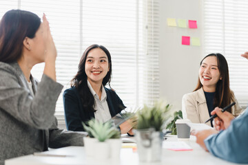 Young Asian businesswomen in modern office, smiling and discussing ideas with teamwork, casual meeting atmosphere, creative collaboration, positive energy