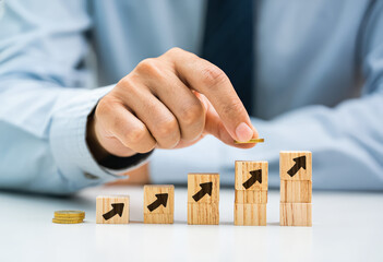 Businessman placing wooden block with upward arrow on stacked coins for financial growth concept