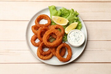 Fried squid rings, lemon, lettuce and sauce on light wooden table, top view