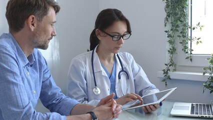 Female doctor using a digital tablet for explaining test results to a male patient during a...