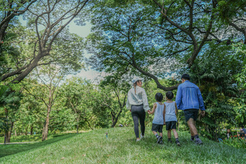 A happy Asian family with two young sons enjoys a walk in the park. Parents hold their children's hands while exploring a lush green hill together, a concept of family bonding.