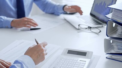 Two accountants collaborating in a bright office, analyzing financial documents and using a calculator with a laptop displaying charts. Audit and taxes in business