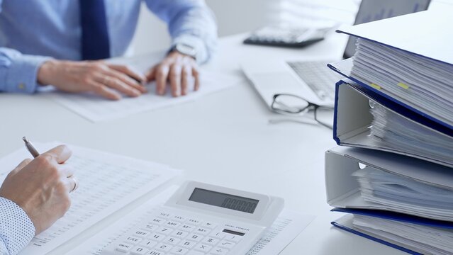 Two accountants collaborating in a bright office, analyzing financial documents and using a calculator with a laptop displaying charts. Audit and taxes in business