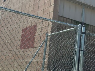 Obraz premium Chain Link Fence and Industrial Brick Wall with Red Patch and Metal Siding – Urban Barrier Scene