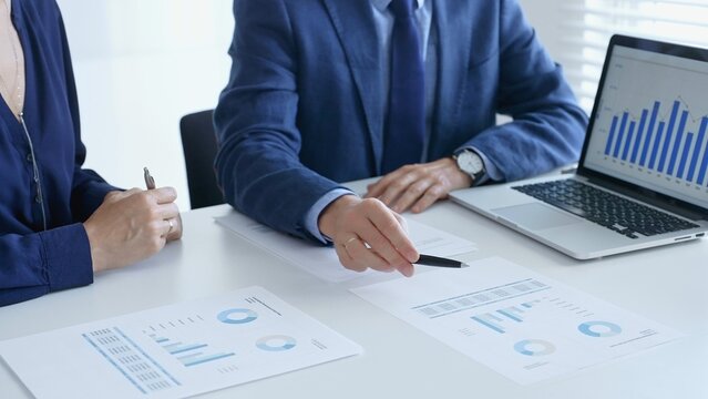 Business professionals reviewing financial data, pointing at laptop charts and shared documents during collaborative strategy session. Business people and finance concept