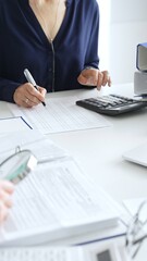 Female financial analysts examining documents, using magnifying glass and calculator while studying corporate data at workplace. Audit and taxes