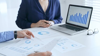 Business professionals collaborating on a laptop, reviewing financial documents, and discussing project strategies in a modern office. Businesspeople in finance concept