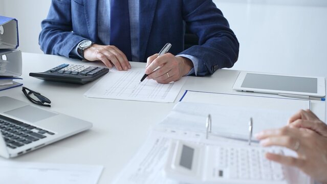 Close up of female accountant hands using calculator while collaborating with male colleague in office, calculating taxes and analyzing financial data. Audit and taxes in business - Powered by Adobe