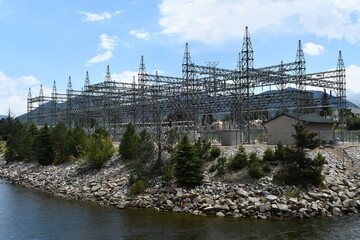 Hydro power facility power grid. Transformers and switching gear. Facility surrounded by water. Beautiful sunny day at the reservoir. Rocky shoreline speckled with pine trees.