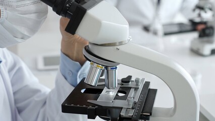 Gloved hands adjusting a microscope in a bright laboratory, emphasizing precision and focus in scientific research. Medicine, healthcare and science concept