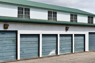 Industrial warehouse with many garage doors. Green metal roofing, white metal siding. Upper portion of building has windows for extra light.