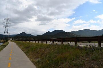 Running path going around large reservoir. Large AC power tower in the distance. Rocky Mountains in background. Highway barrier on one side.