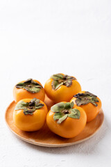 Fresh ripe persimmon on wooden plate with white background, Autumn sweet fruit