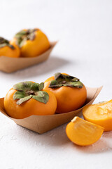 Fresh ripe persimmon in paper bowl on white background, Autumn sweet fruit