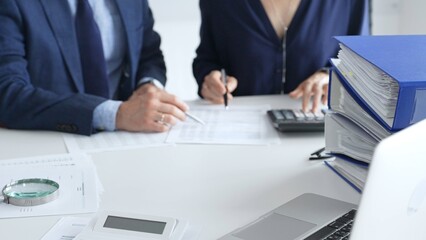 Close up of magnifying glass and calculator over financial documents opposite financial team, reviewing reports, collaborating on accounting details at modern office workspace. Audit and taxes