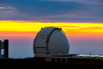 Astronomical observatories atop Mauna Kea, Hawaii, stand above the clouds at sunset, capturing a...