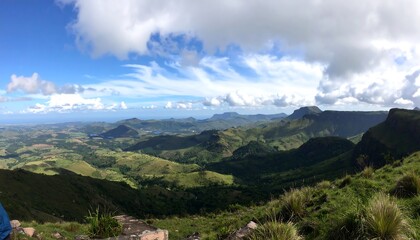 Expansive vista of rolling hills and mountains beneath a dramatic sky, showcasing a rich tapestry of green landscapes.