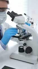 Man scientist wearing protective googles and blue gloves, is using microscope analyzing samples in modern laboratory doing scientific research. Medicine and science concept