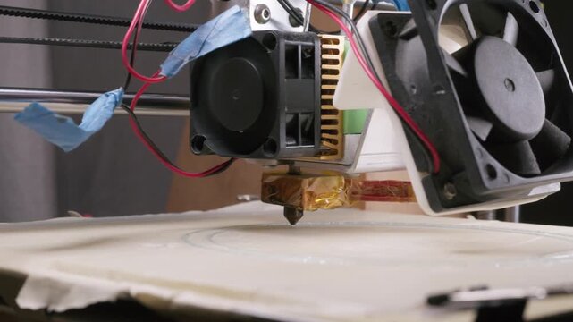 DIY 3d printer in use at home.  Close up shot of home made simple 3d printer, printing a circular object on flat build plate covered with masking tape.  